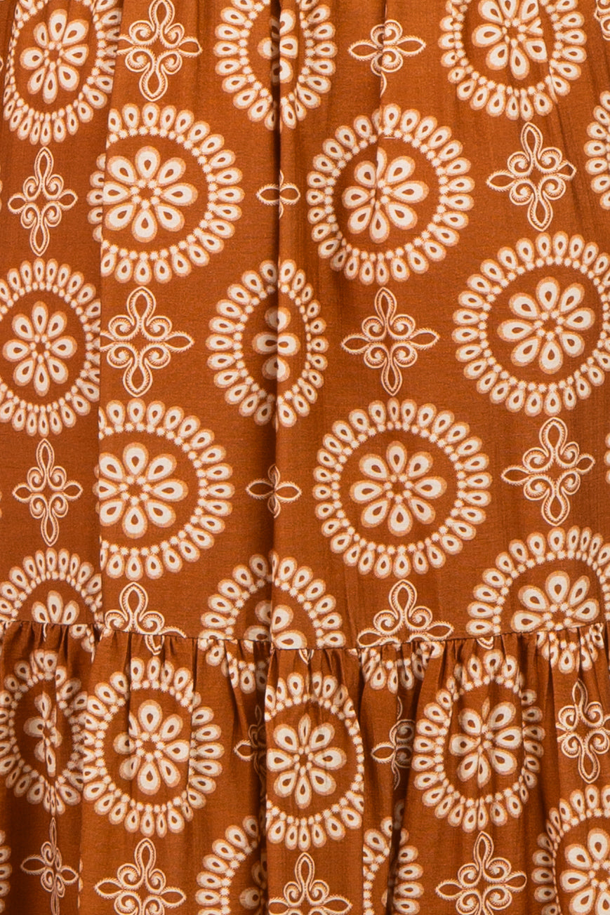 maternity wear in a rust-colored dress featuring a circular floral pattern and a tiered ruffled hem