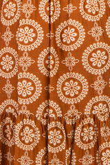 maternity wear in a rust-colored dress featuring a circular floral pattern and a tiered ruffled hem