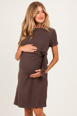 woman wearing a brown short sleeve maternity dress with a tie detail and holding her baby bump