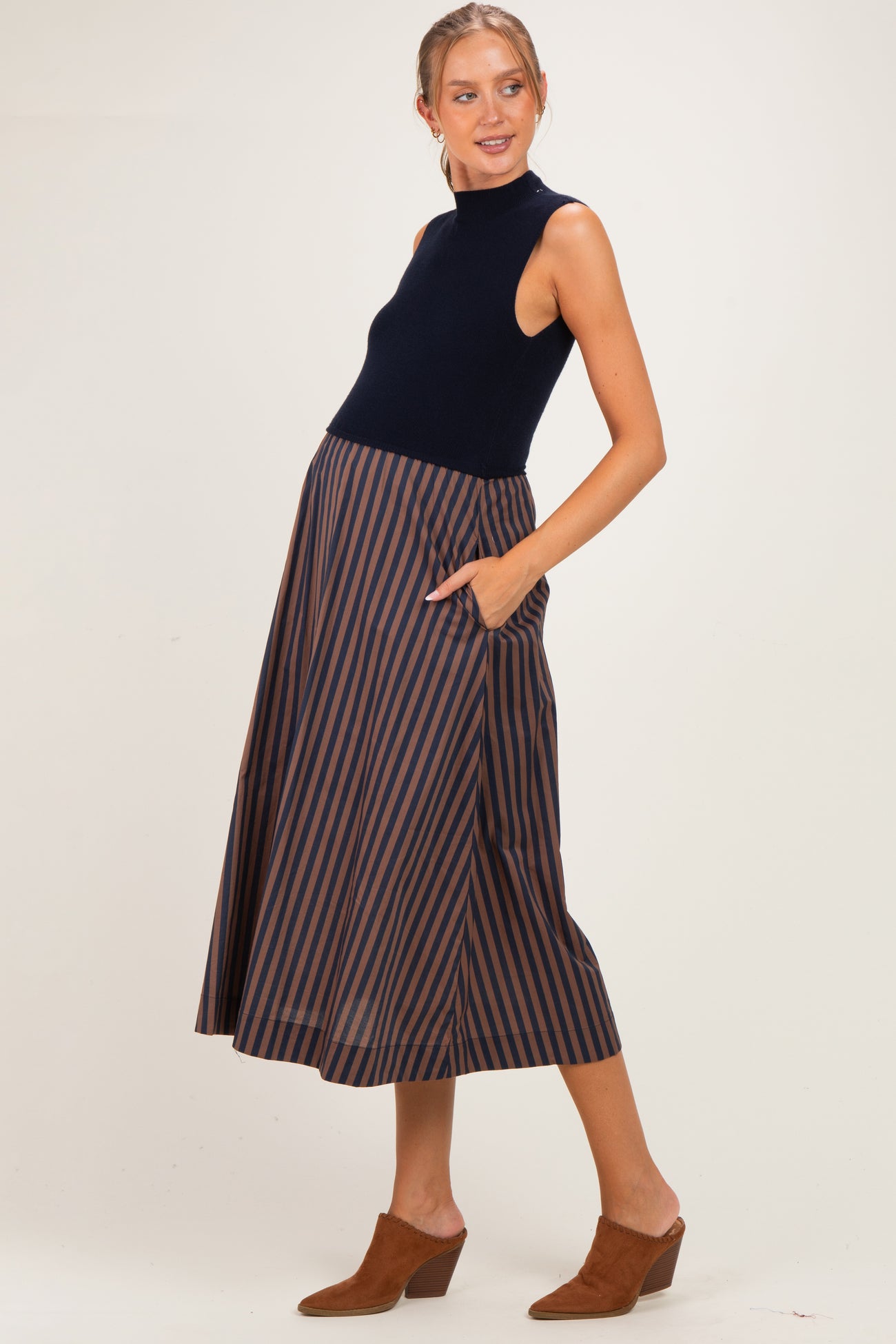 woman wearing a navy sleeveless top and a brown striped maternity skirt with pockets, showcasing her baby bump