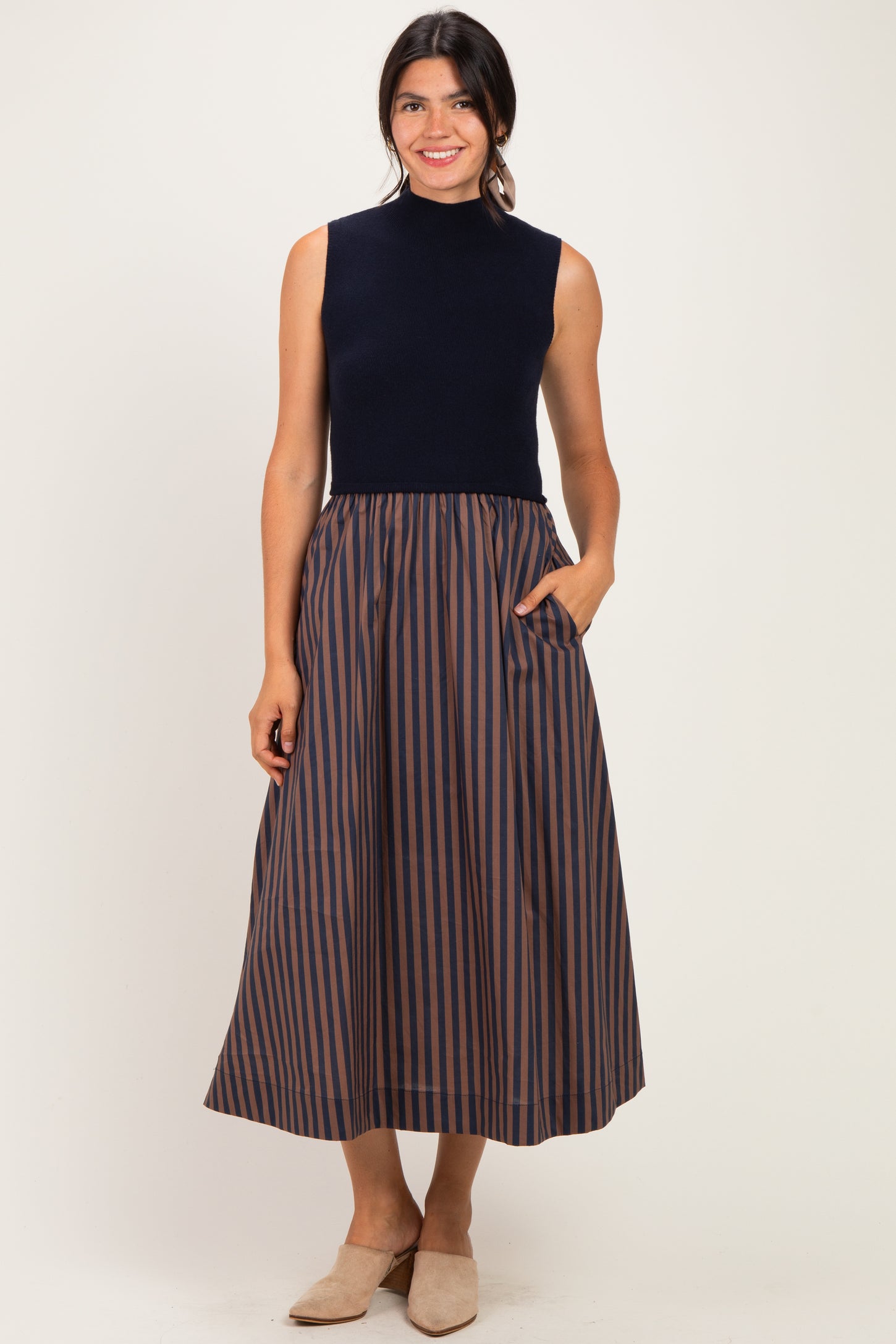 woman wearing a navy sleeveless top and a striped midi skirt with pockets, standing and smiling