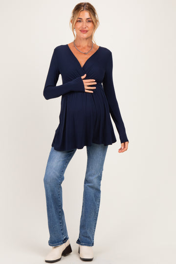 woman wearing a navy blue long sleeve maternity top and holding her baby bump with light blue jeans