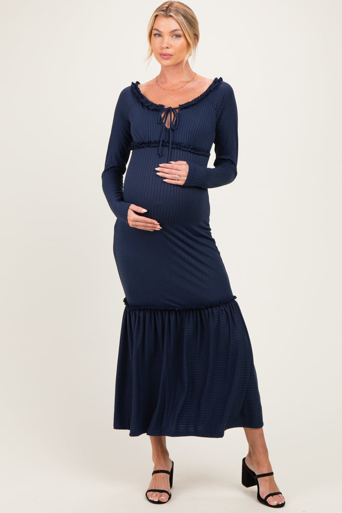 woman wearing a navy blue maternity dress with long sleeves and a ruffled hem, holding her baby bump