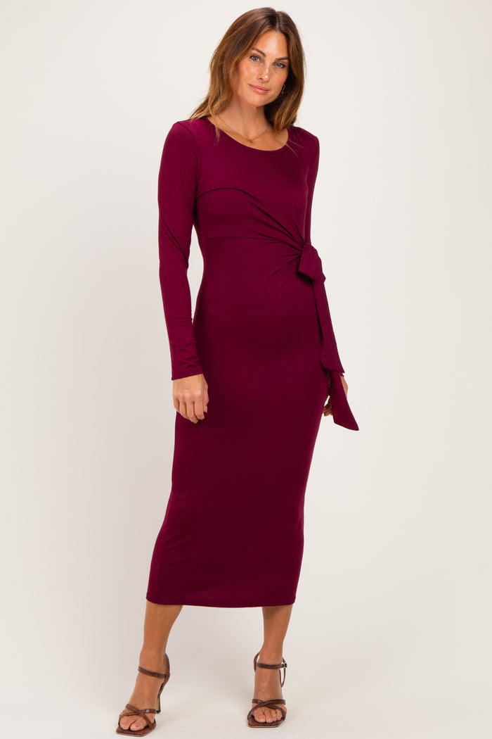woman wearing a burgundy long sleeve midi dress with a twist detail at the waist and strappy heels
