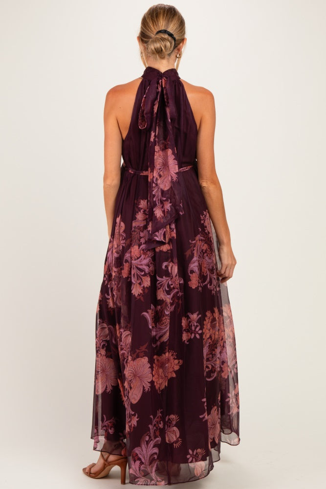 woman wearing a long purple floral maternity dress with a halter neck and flowing sheer skirt from the back