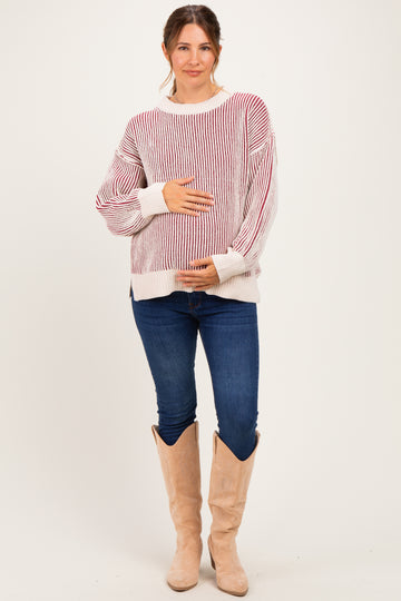 woman wearing a striped red and white maternity sweater and blue jeans, holding her baby bump