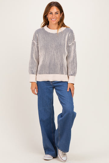 woman wearing a striped oversized sweater in cream and black with high-waisted flared jeans and sneakers