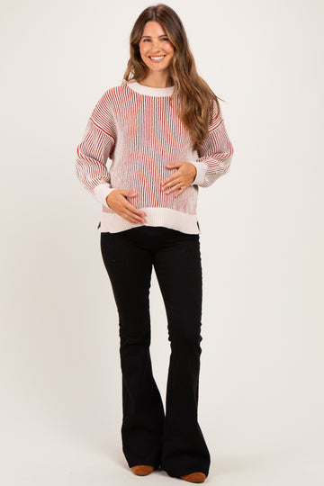 woman wearing a red and white striped maternity sweater and holding her baby bump, paired with black flared pants