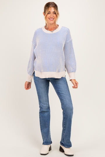 woman wearing a blue and white striped maternity sweater with balloon sleeves and light wash jeans, smiling at the camera