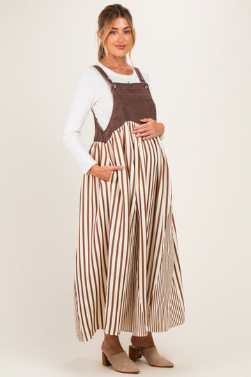 woman wearing a brown and white striped maternity dress with adjustable straps and pockets, showcasing her baby bump