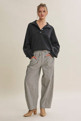woman wearing a black quarter-zip pullover and gray striped wide-leg pants with pockets, standing in beige heels