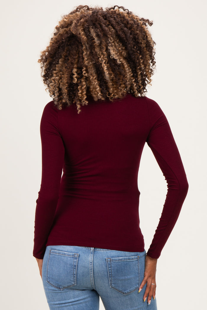woman wearing a burgundy long sleeve maternity top, showing the back view, paired with blue jeans