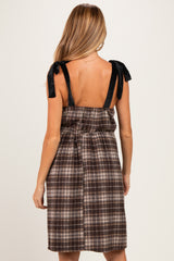 woman wearing a brown plaid maternity dress with black bow straps and a cinched waist