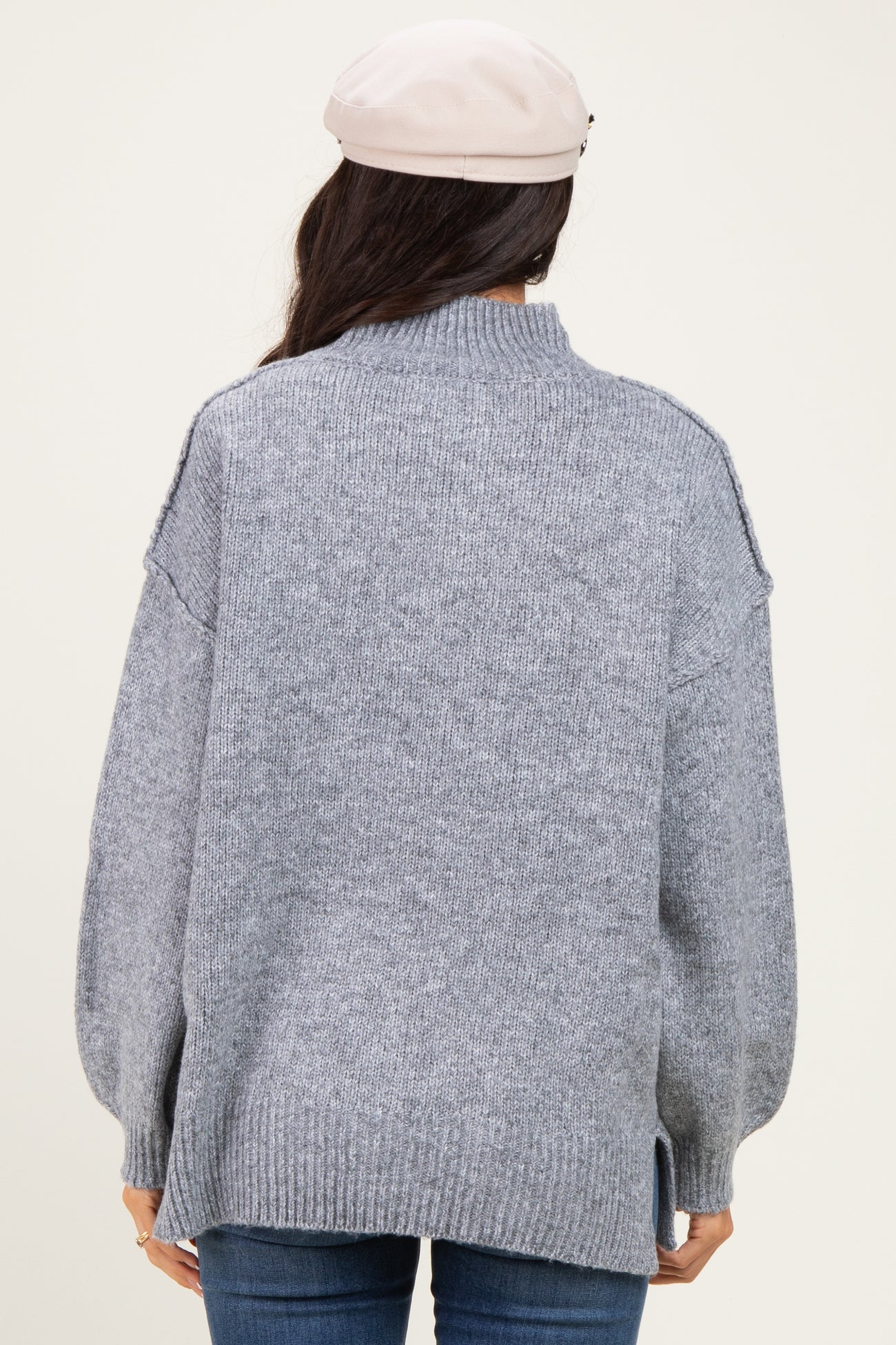 woman wearing a gray oversized turtleneck sweater with side slits and relaxed fit from the back