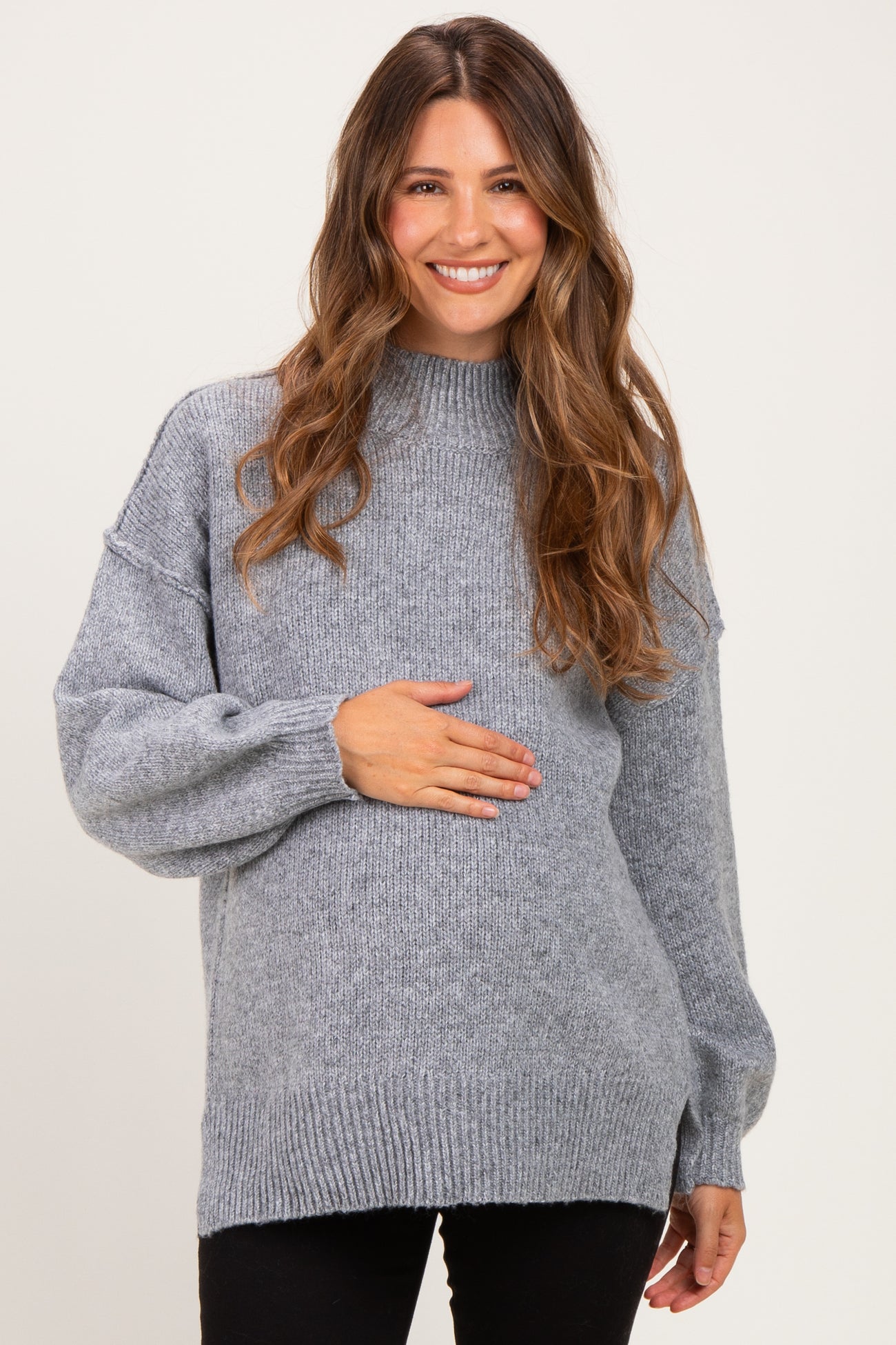 woman wearing a gray maternity sweater with a high neck and long sleeves, holding her baby bump