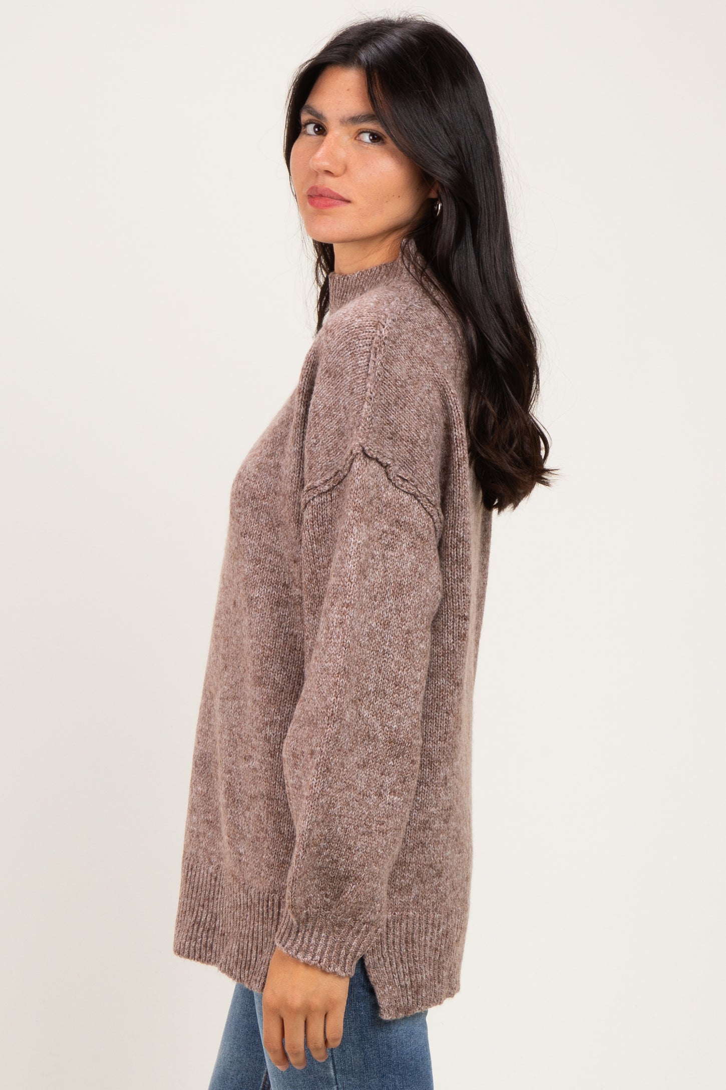 woman wearing a taupe oversized sweater with a mock neck and ribbed hem, styled with blue jeans