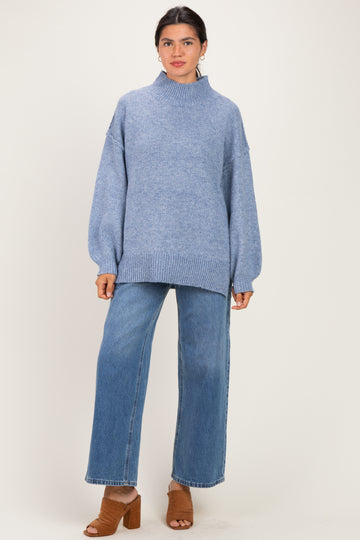 woman wearing a light blue oversized sweater with a mock neck and wide-leg jeans, standing in brown block-heeled sandals