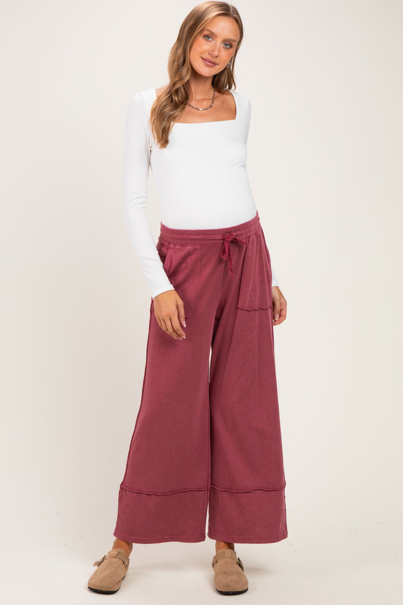 woman wearing a white long sleeve maternity top and burgundy wide-leg maternity pants with pockets and a drawstring