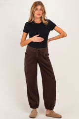 woman wearing a black short sleeve maternity top and brown maternity jogger pants, holding her baby bump