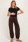 woman wearing a black short sleeve maternity top and brown maternity jogger pants, holding her baby bump