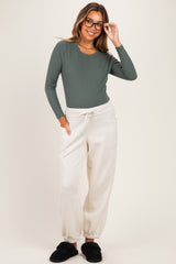 woman wearing a dark green long sleeve maternity top and light beige maternity joggers, smiling with glasses