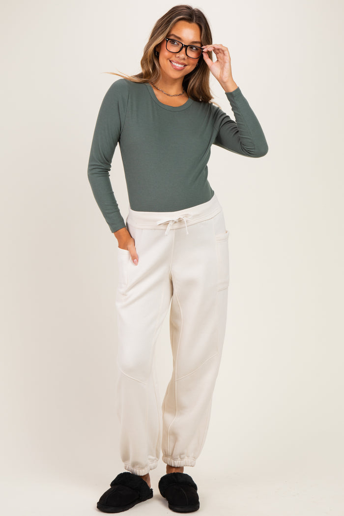 woman wearing a dark green long sleeve maternity top and light beige maternity joggers, smiling with glasses