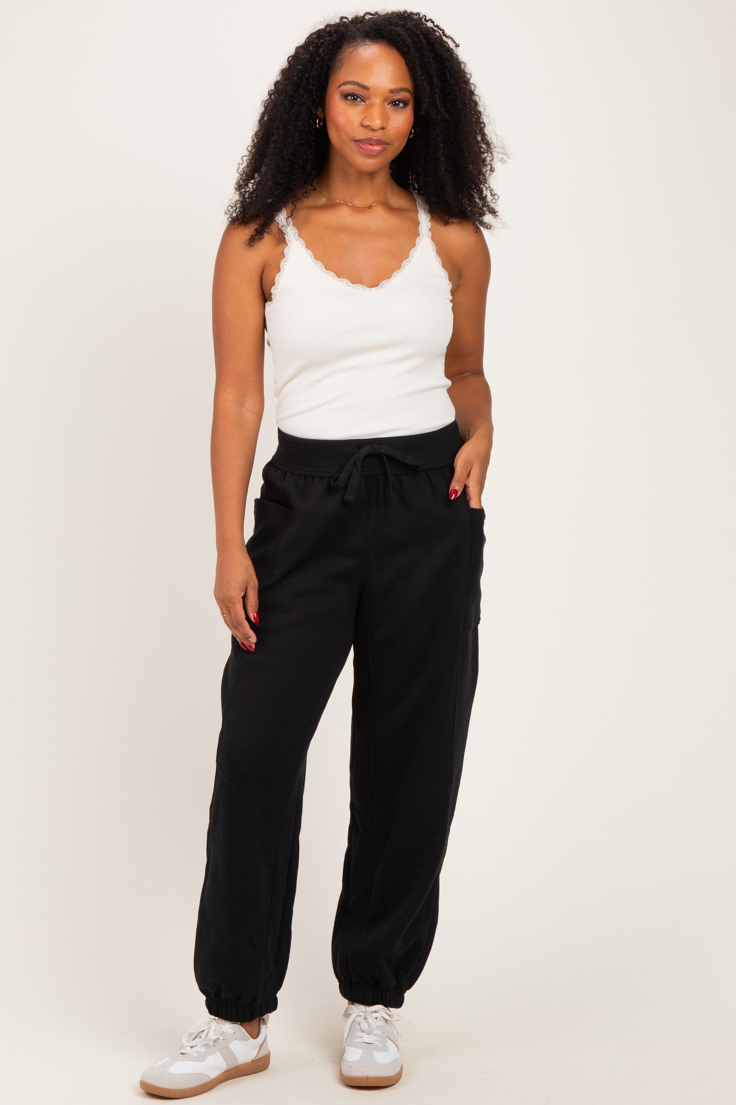 woman wearing a white sleeveless top and black jogger pants, standing and looking at the camera
