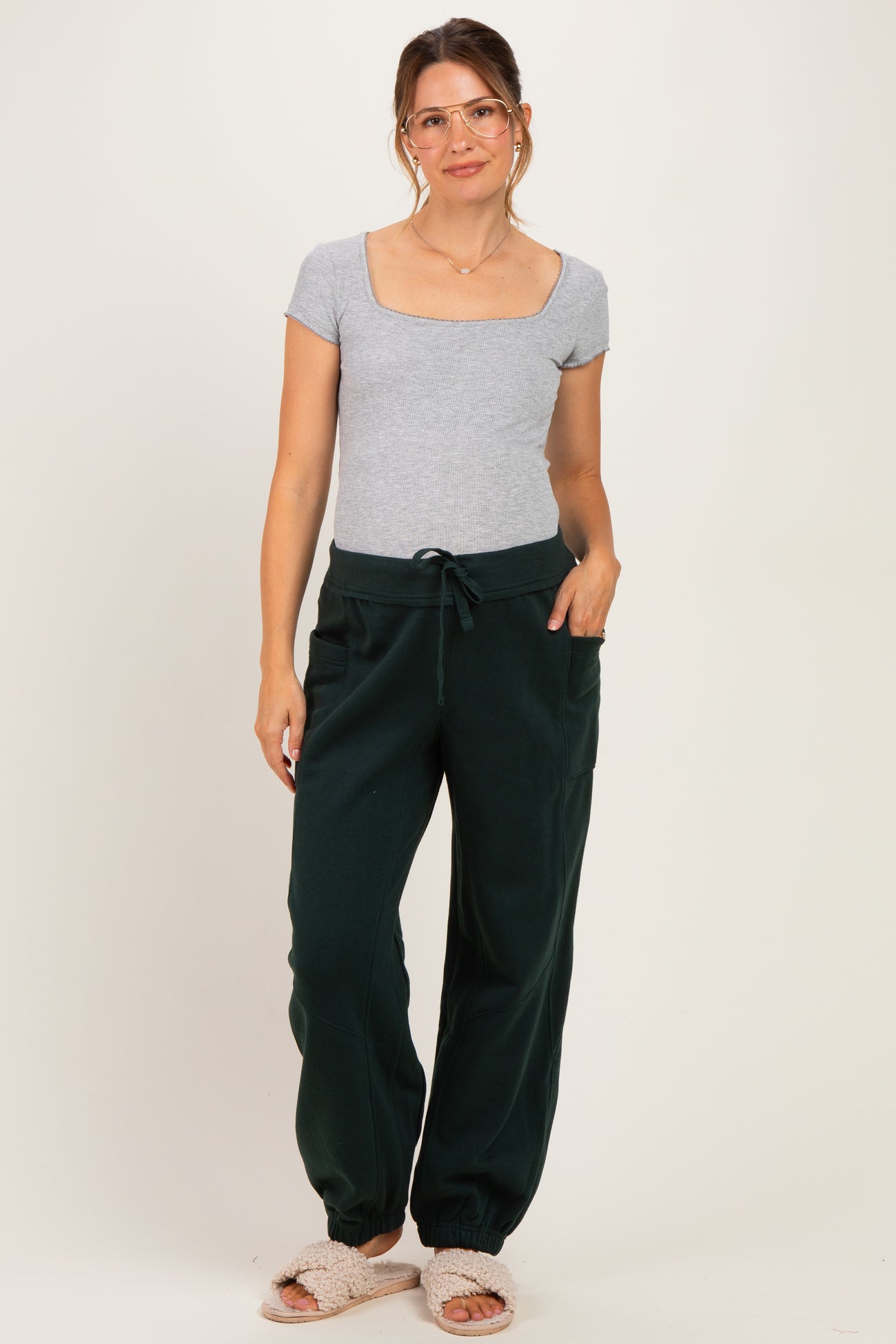 woman wearing a gray short sleeve maternity top and green maternity jogger pants, styled with light footwear and glasses