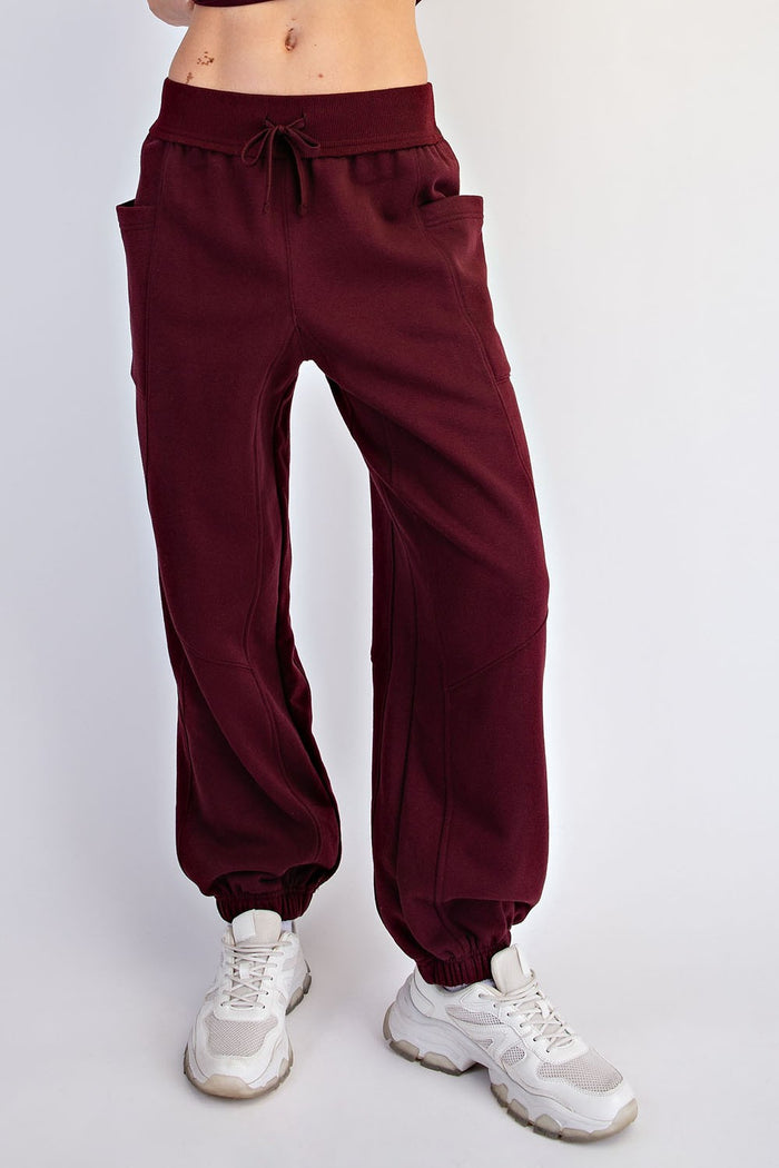 woman wearing burgundy jogger pants with pockets and cuffed ankles, styled with white sneakers