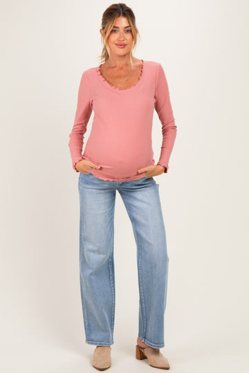 woman wearing a pink long sleeve maternity top with ruffle detailing and jeans, holding her baby bump