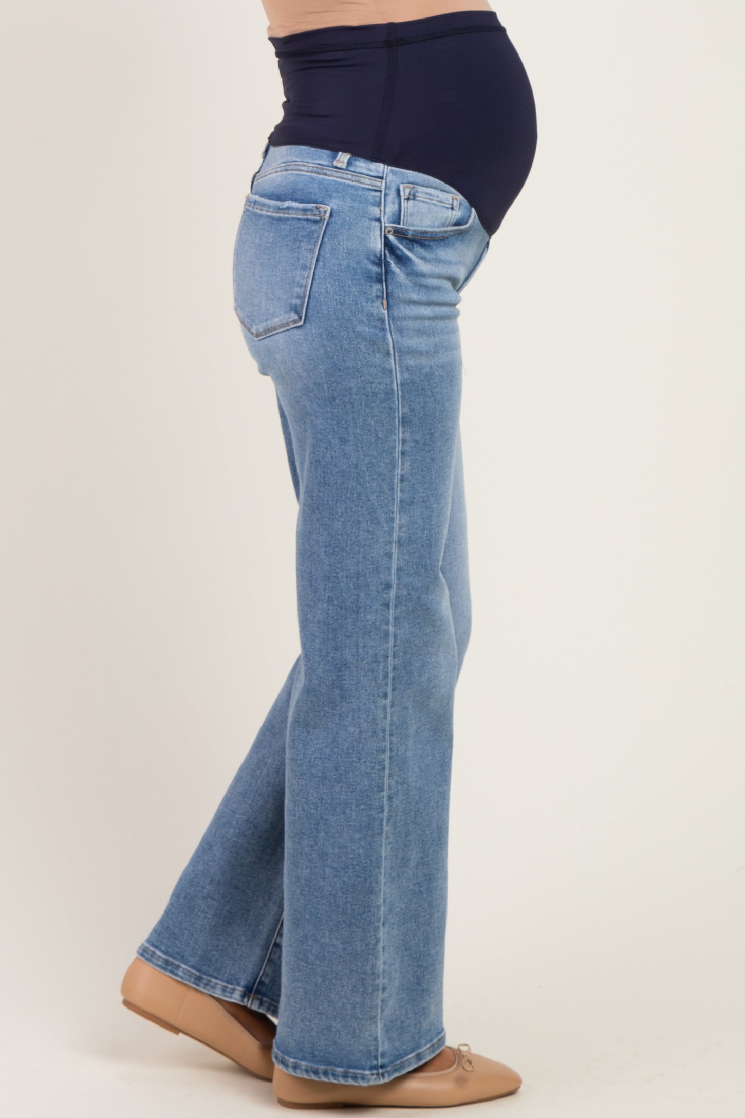 woman wearing light wash maternity jeans with a supportive belly band and visible baby bump.