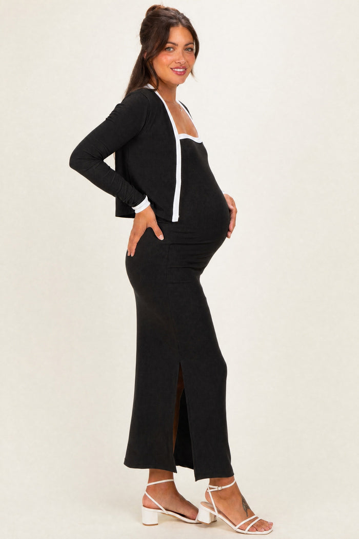 woman wearing a black maternity dress with a side slit and a matching open cardigan, gently cradling her baby bump