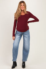 woman wearing a burgundy long sleeve maternity top and light wash wide-leg jeans, showing her baby bump