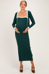 woman wearing a dark green maternity dress with a white bodice detail and a matching cardigan, showing her baby bump