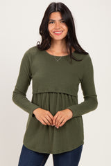 woman wearing a dark green long sleeve ribbed top with a fitted bodice and flowy bottom, smiling at the camera