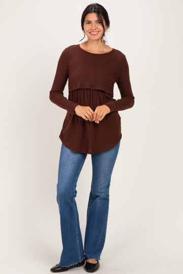 woman wearing a brown long sleeve top with a peplum waist and flared jeans, standing and smiling at the camera