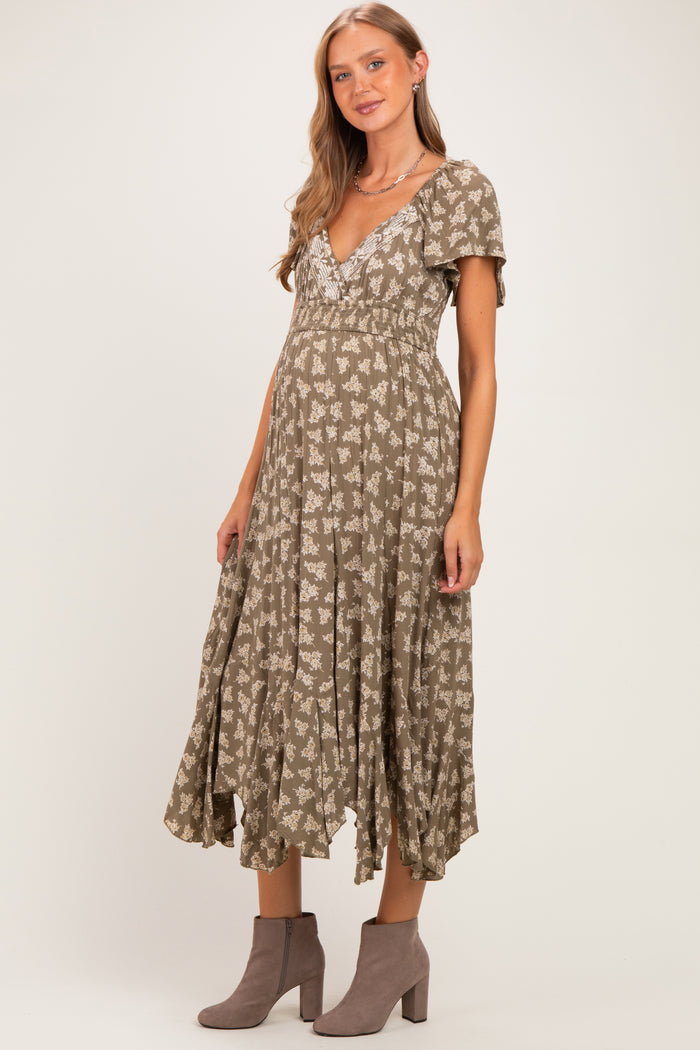 woman wearing a sage green floral maternity dress with short sleeves and a flowy skirt, showing her baby bump