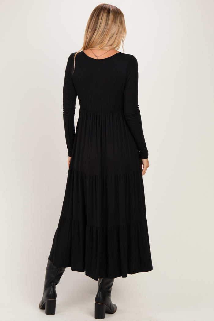 woman wearing a black long sleeve maxi dress with a tiered skirt and a fitted bodice, seen from the back