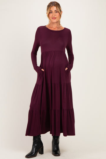 woman wearing a dark purple long sleeve maternity dress with tiered design and pockets, showcasing her baby bump