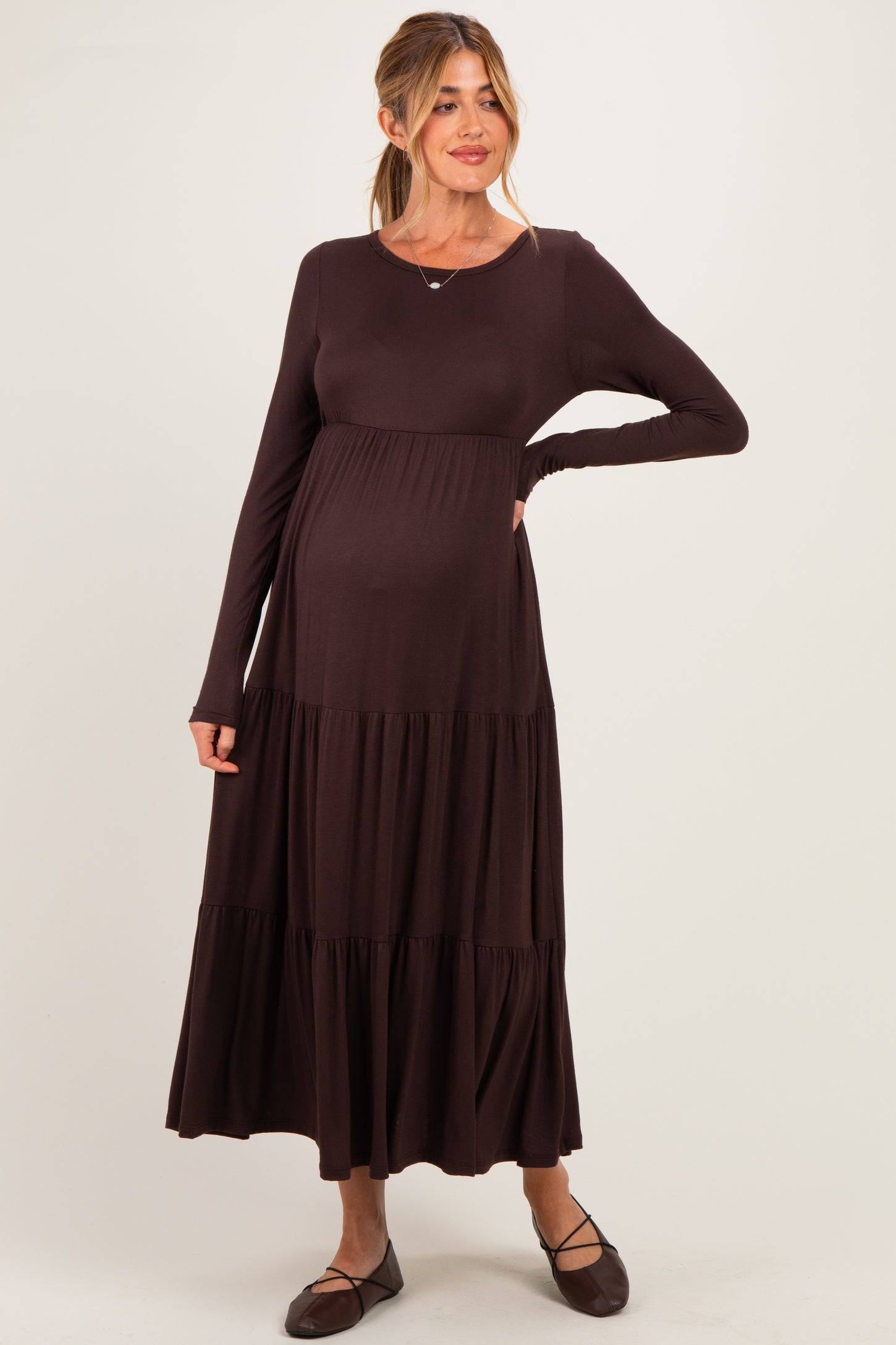 woman wearing a dark brown long sleeve maternity dress with tiered skirt and visible baby bump