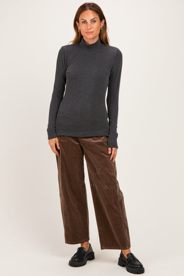woman wearing a gray ribbed long sleeve top and brown wide-leg corduroy pants, standing against a light background