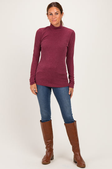 woman wearing a maroon ribbed turtleneck sweater with long sleeves and blue skinny jeans, standing in knee-high brown boots
