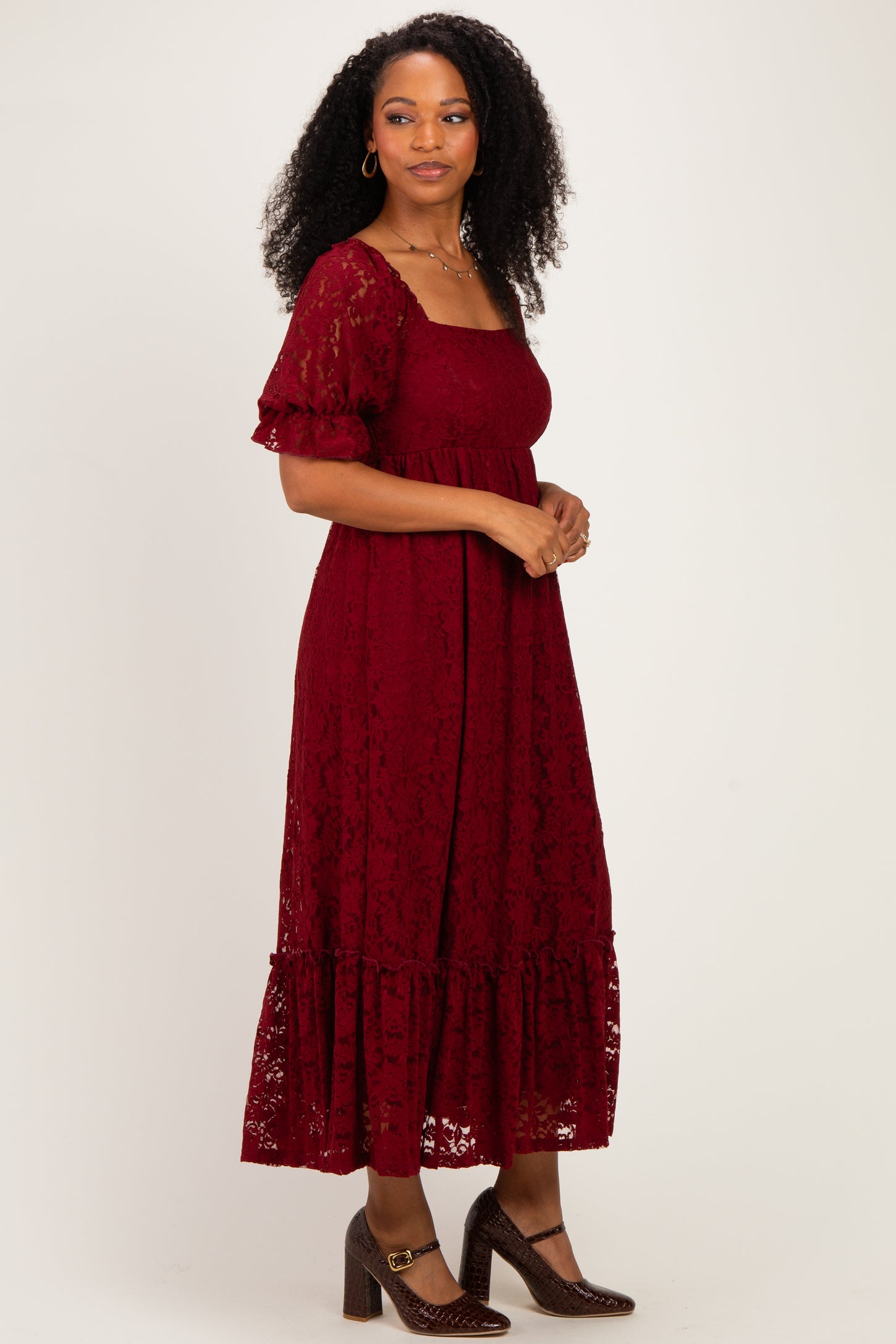 woman wearing a burgundy lace maxi dress with short sleeves and a ruffled hem, standing against a neutral background