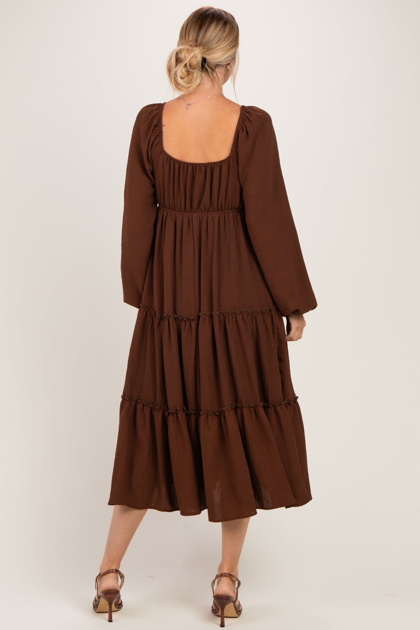 woman wearing a brown tiered midi dress with long sleeves and a square back revealing the shoulder and upper back
