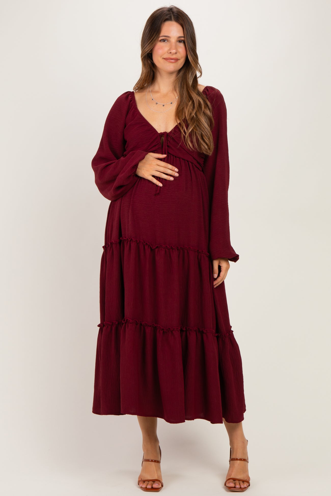 woman wearing a burgundy maternity dress with long sleeves and tiered ruffles, holding her baby bump