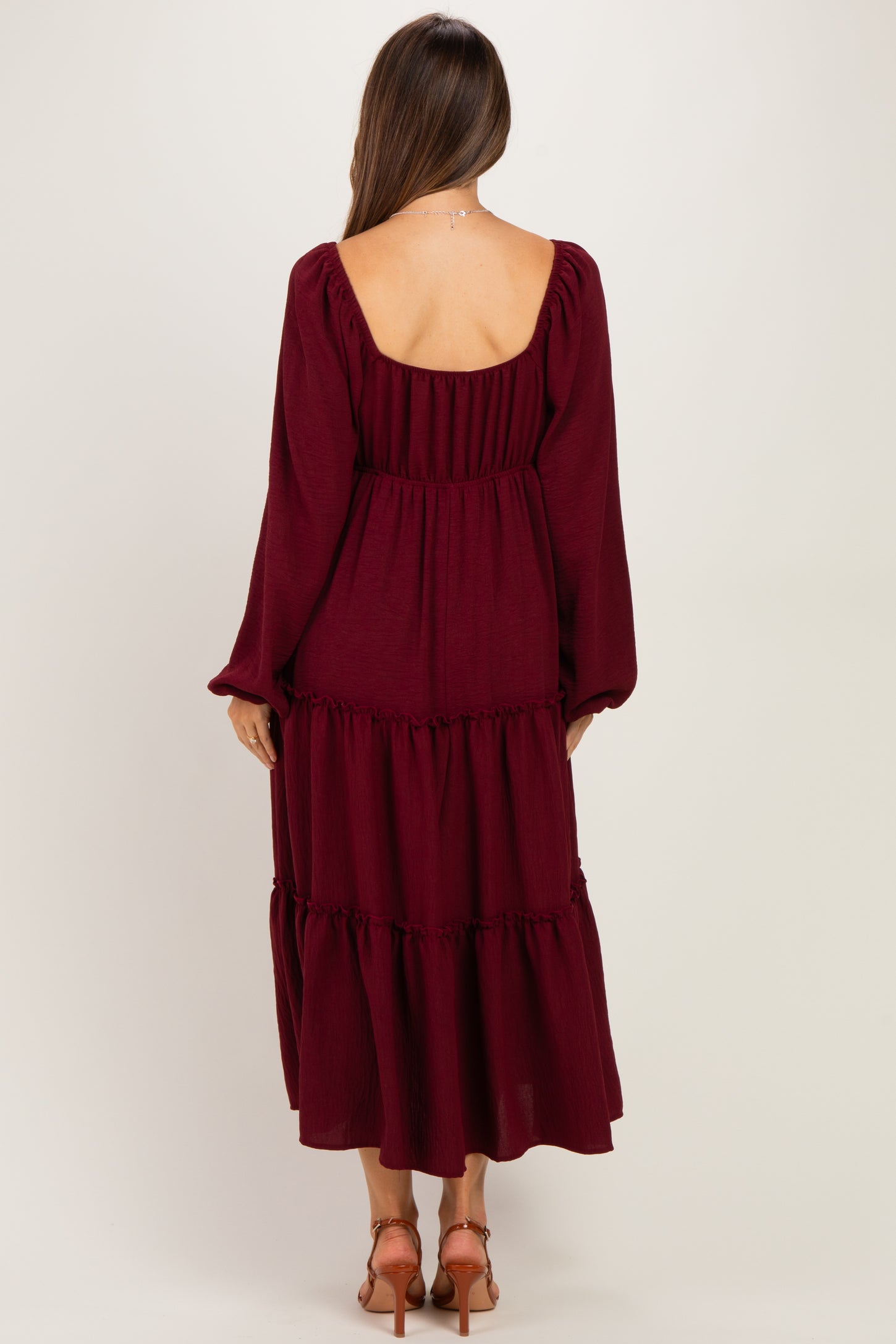 woman wearing a burgundy maternity dress with long sleeves and a tiered skirt, showing a scooped back design