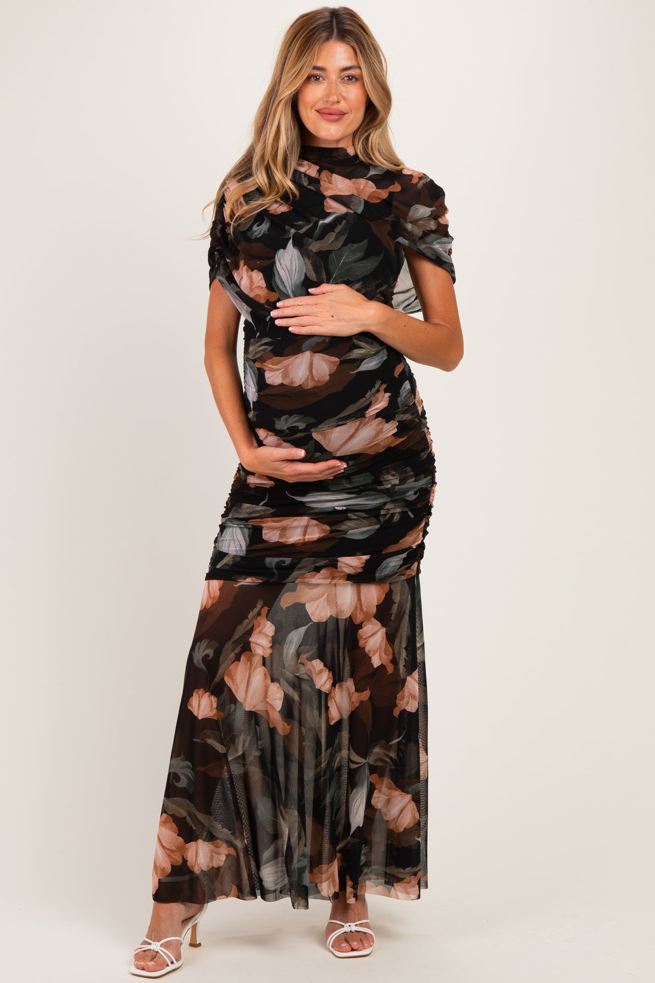 woman wearing a black floral print maternity dress with ruching and a flowing skirt, cradling her baby bump