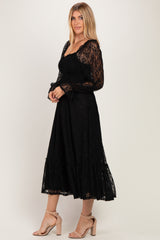 woman wearing a black lace long sleeve dress with a smocked bodice and tiered skirt, standing sideways