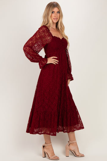woman wearing a burgundy lace midi dress with long puff sleeves and a tiered skirt, standing in a side pose