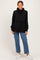 woman wearing a black cropped hoodie with long sleeves and a relaxed fit, styled with high-waisted blue jeans and white sneakers